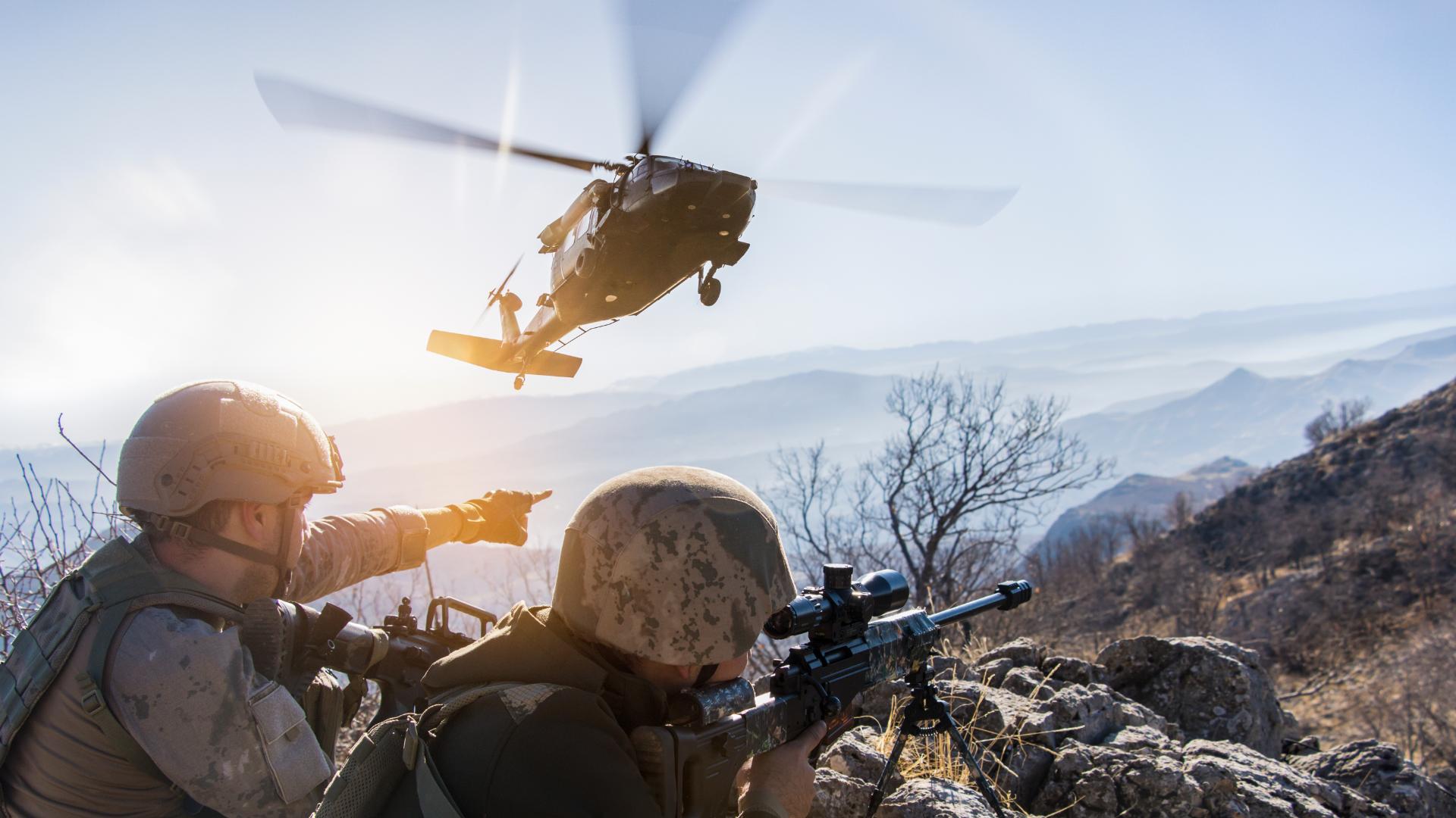 foto de militares em missão com um helicóptero ao fundo.